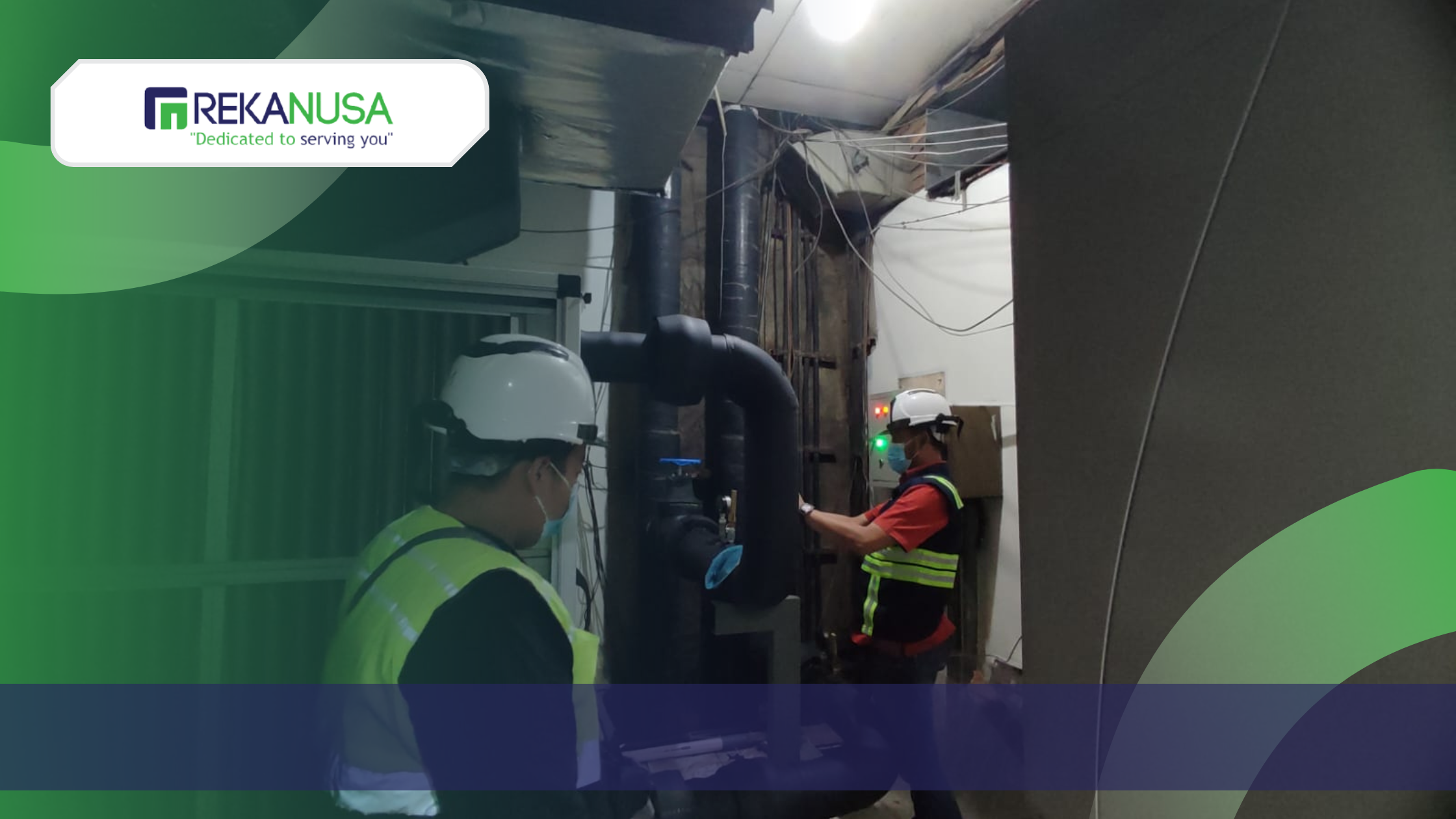 Dua orang teknisi dari Rekanusa mengenakan helm dan rompi keselamatan sedang melakukan inspeksi teknis pada sistem perpipaan industri dan panel kontrol listrik di dalam area utilitas gedung.